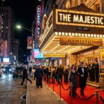 Glamorous nighttime view outside a historic Broadway theater in Times Square with glowing marquee lights and elegant theatergoers
