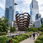 Stunning view of The Vessel bronze honeycomb structure framed by modern glass skyscrapers and lush gardens of The High Line