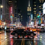 Atmospheric nighttime cityscape of Manhattan illuminated by Times Square neon lights with private executive car